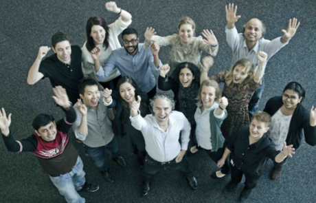 A high-angle view looking down at the lab memebers with Christopher Pearson as they cheer and wave their hands in the air.