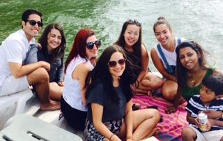 Group of eight people, including a young child, sitting together on a deck on a green-colored body of water, smiling at the camera.