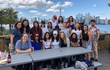 Group of people wearing t-shirts and shorts, sitting and standing behind a picnic table in front of the Toronto skyline