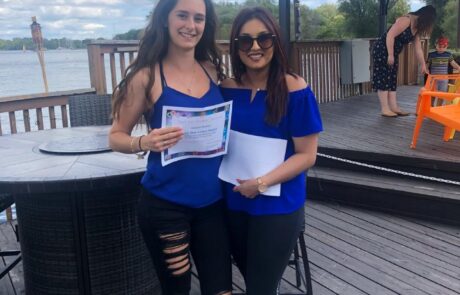 Two people standing on a desk each holding a certificate and smiling at the camera