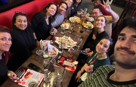 Group of people sitting at a dinner table in a restaurant, smiling and posing for a selfie.