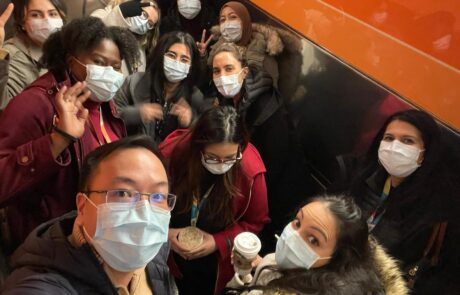 Group of people in winter coats and masks standing and looking at the camera for a selfie.