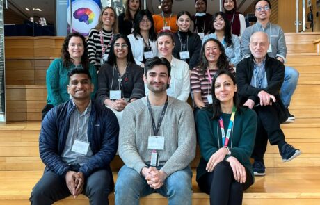 Group of diverse researchers and students wearing lanyards sitting on wooden steps, smiling at the camera