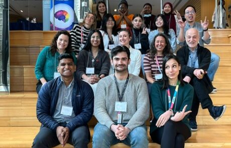 Group of diverse researchers and students wearing lanyards sitting on wooden steps, making silly faces at the camera