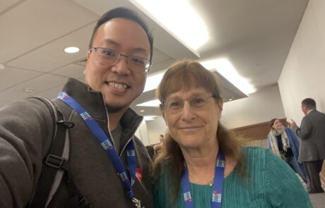 Selfie with two people wearing lanyards smiling at the camera.