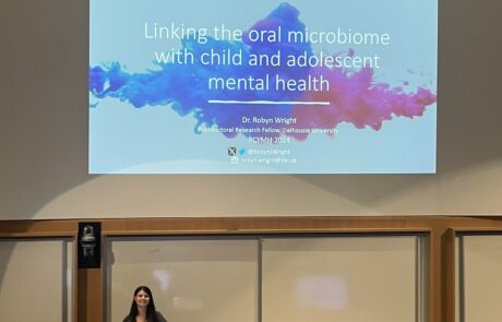 Young woman behind a podium with slides projected behind her titled "linking the oral microbiome in children and adolescent mental health"