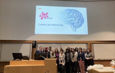 Group of researchers and students in a lecture hall under a projected presentation slide titled "Crosbie Lab Science Day"