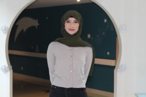Ayeza standing in a hallway, smiling with her arms behind her back.