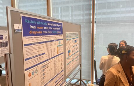 Two posters on a board, one titled racial/ethnically marginalized youth had lower odds of a psychaitric diagnosis than their white peers. Three people on the side looking at surrounding posters.