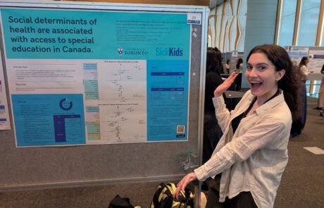 Woman with long brown curly hair in a ponytail smiling and pointing to a poster on her right titled "Social determinants of health are associated with access to special education in Canada".