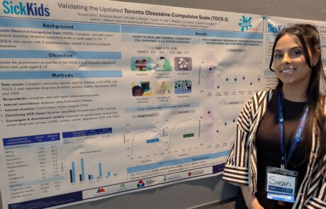 Woman with long black hair and striped shirt standing beside a research poster titled "Psychometric properties and age extension of the revised child anxiety & depression scale 25 in a canadian population".