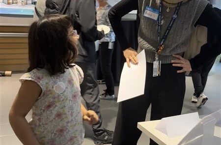 A little girl looking up at a woman while standing on a balance beam. They are both smiling at each other.