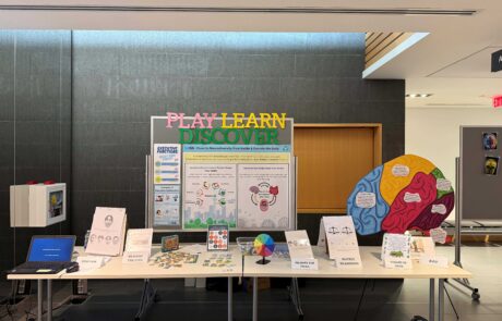 A science fair booth titled "play, learn, discover" with various posters, infographics and games about cognition, the environment, and the microbiome.
