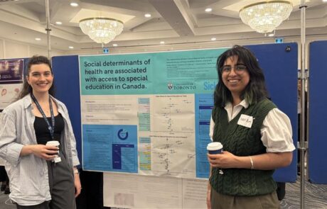 Two woman stand on either side of a research poster, smiling at the camera.