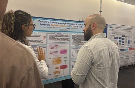 Two people looking at a research poster. A woman is talking to a man on her right explaining the poster.