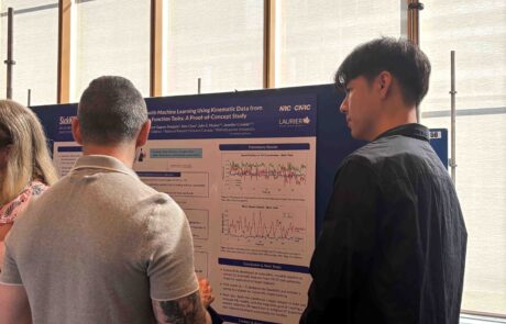 Two men look at a research poster. One is looking at the poster, the other is looking at the man.