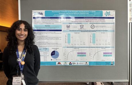 Girl with lanyard and black curly hair standing beside a blue and white research poster, smiling at the camera