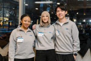 Three people in matching grey quarter-zip sweaters stand beside each other, smiling at the camera.