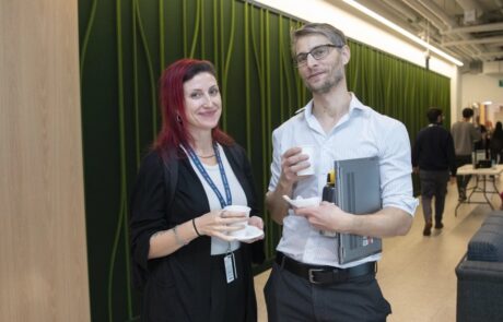 A man and woman wearing lanyards, stand next to each other, smiling at the camera.