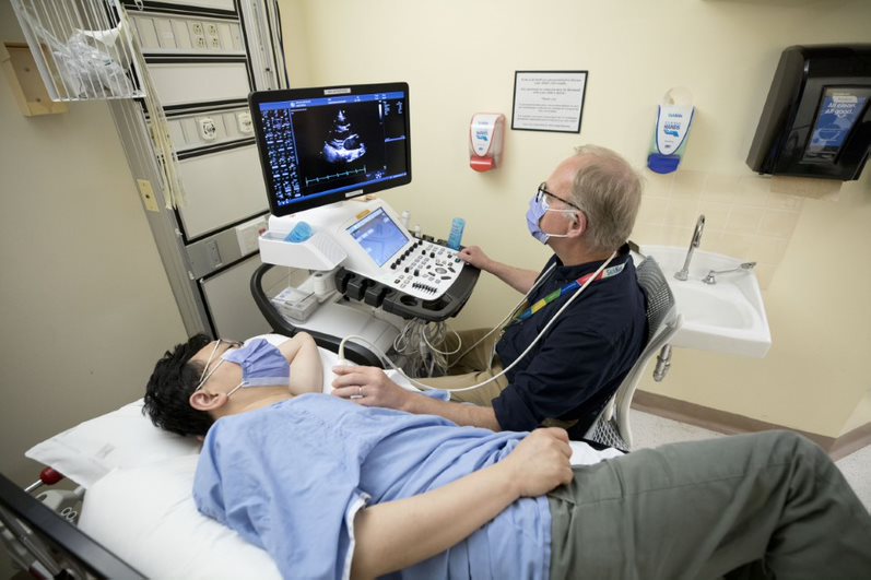 A sonographer performs the cardiac ultrasound scan on a patient who is lying on their left side.