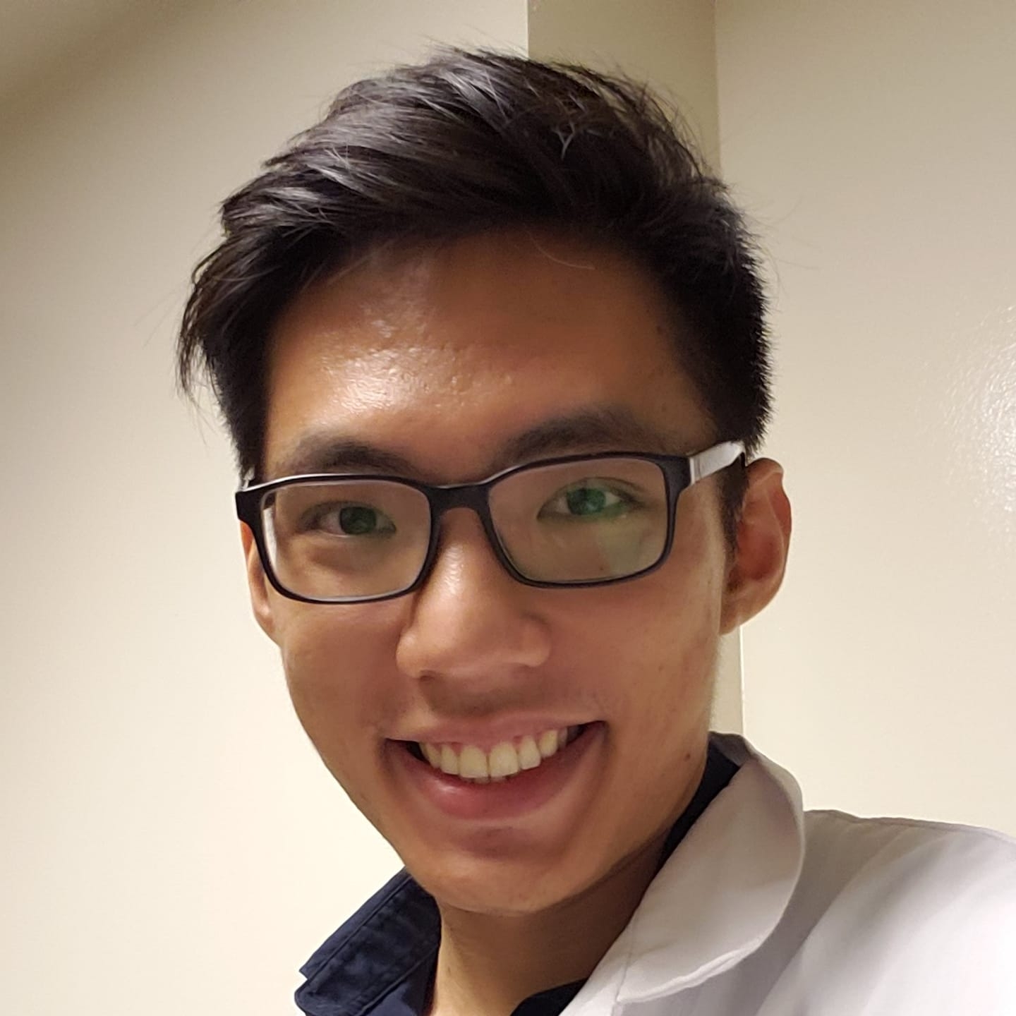 Smiling south east Asian male wearing glasses and a lab coat.