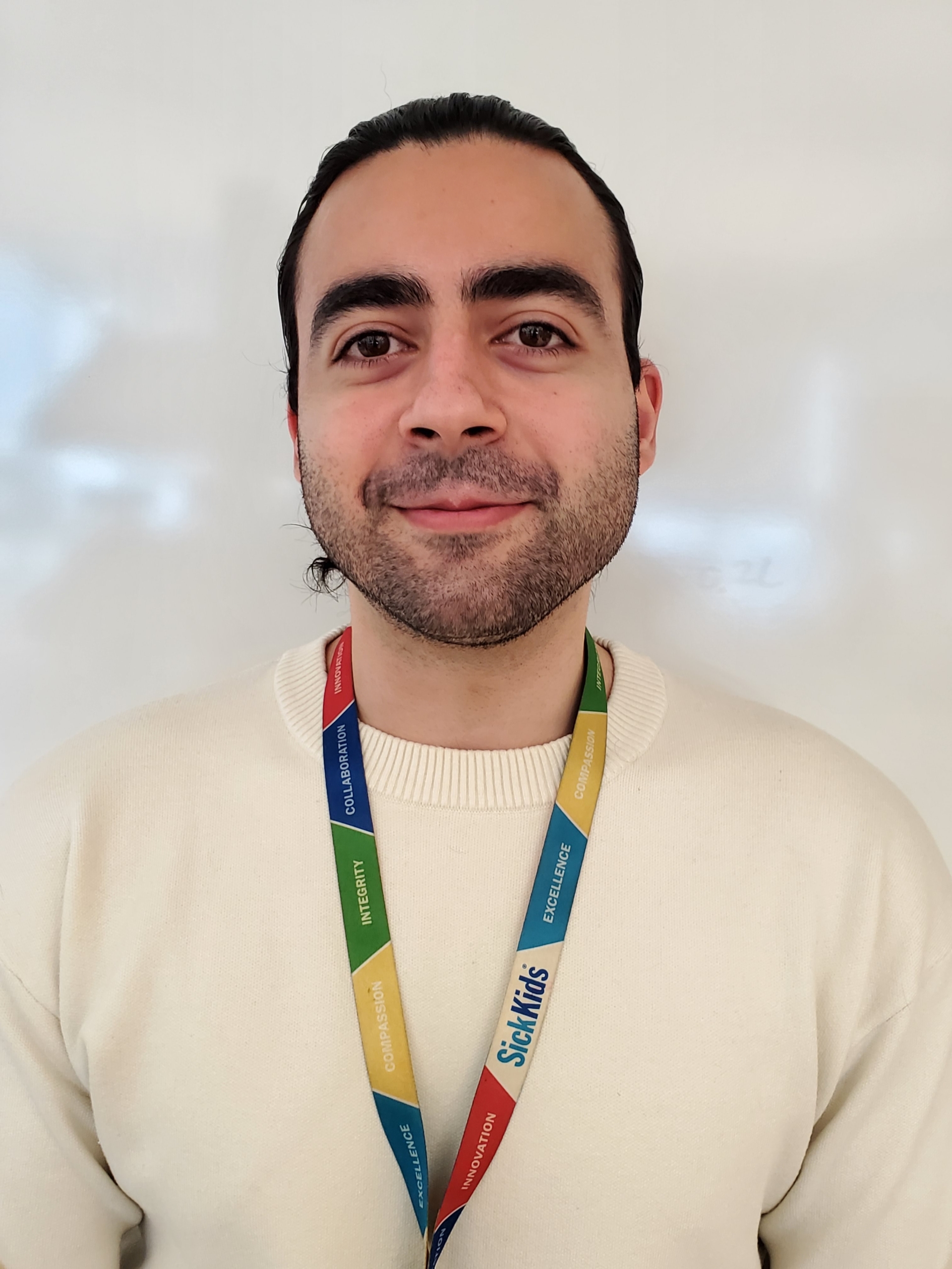 Smiling caucasian male with a 5'o clock shadow, wearing an official lanyard and white sweater.