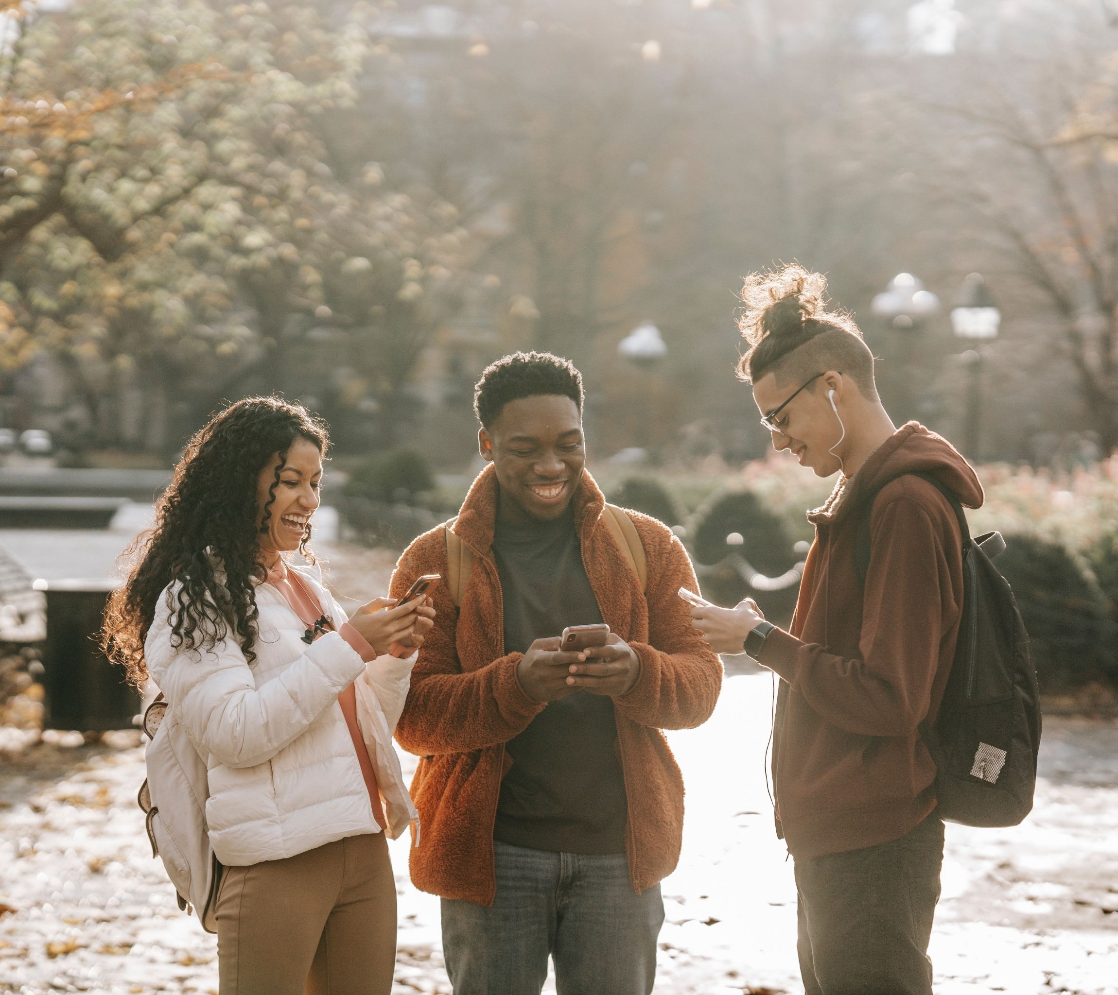 multiracial students using phones and laughing in a city park