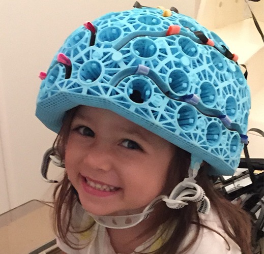 Child smiling, wearing a blue OPM-MEG helmet