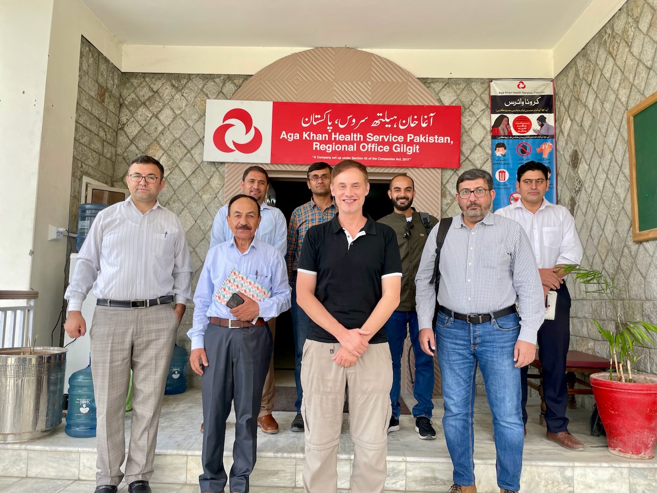 Dr. Morris posing for a photo with a group of seven other individuals. The banner behind them reads, "Aga Khan Health Service Pakistan, Regional Office Gilgit".