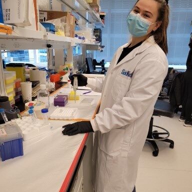 Savina in a lab coat and mask, posing for the camera during a SYTOX Green Assay experiment.