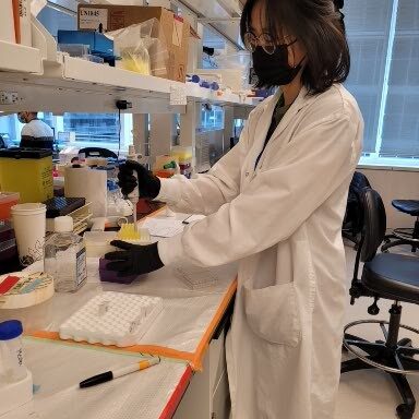 Jessica in a lab coat and mask, doing some pipetting for her experiment