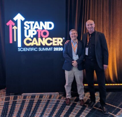 Dr. Uri Tabori and Dr. Daniel Morgenstern posing in front of the SU2C Scientific Summit 2020 Logo