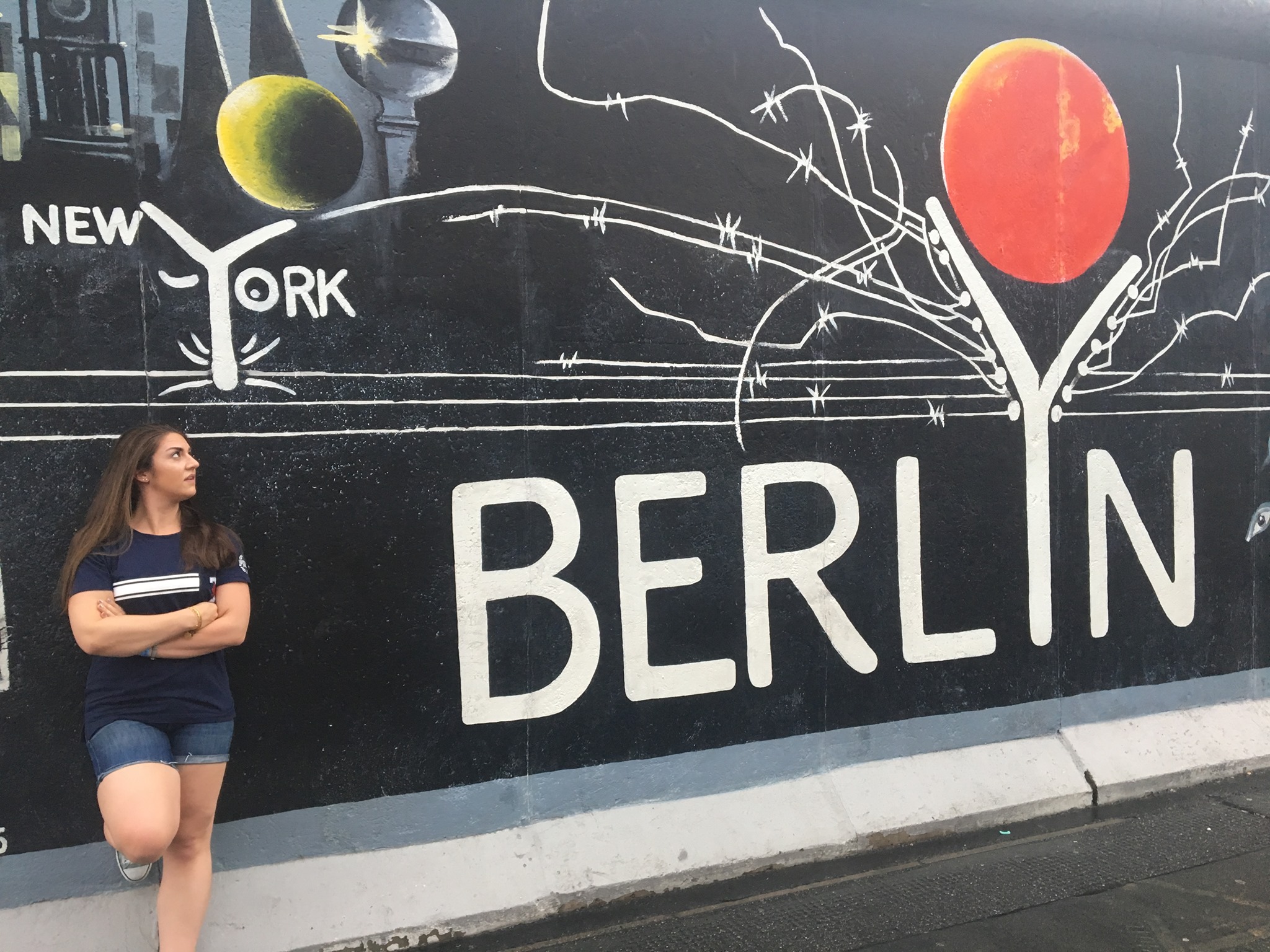 A photograph of Alexxandra Riemenschneider leaning against a mural on the streets of Berlin.