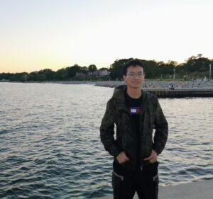 Muyang Cheng Headshot Muyang standing in front of a lake with a sunset in the background